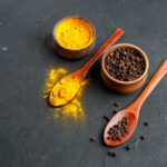 زردچوبه و فلفل سیاه در کاسه و قاشق چوبی