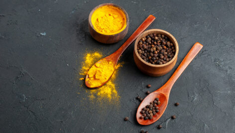 زردچوبه و فلفل سیاه در کاسه و قاشق چوبی