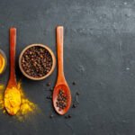 زردچوبه و فلفل سیاه در کاسه و قاشق چوبی
