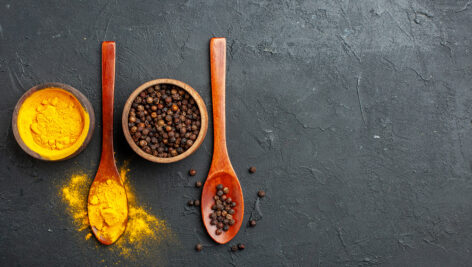 زردچوبه و فلفل سیاه در کاسه و قاشق چوبی